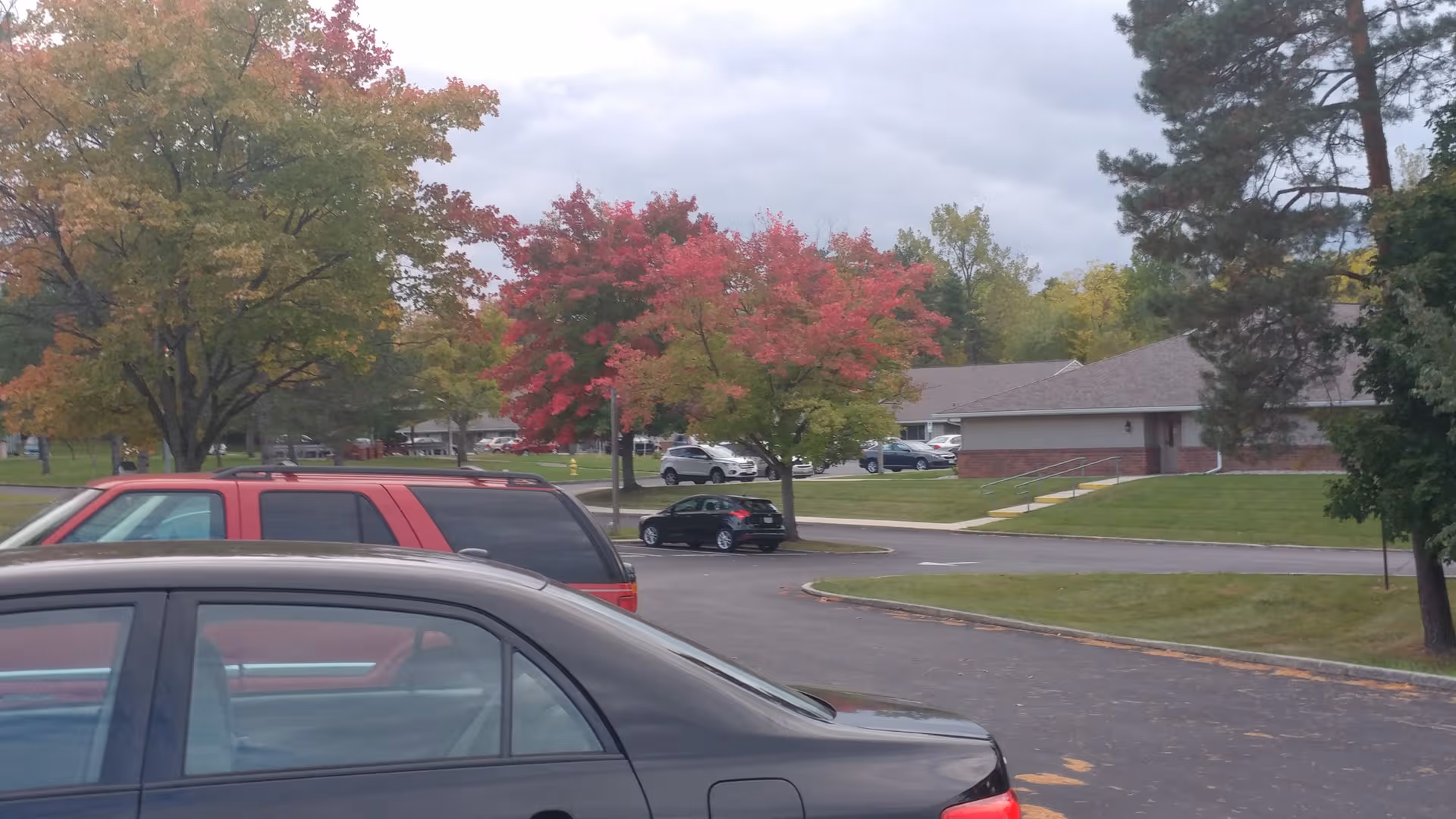Parking lot and facility exterior with autumn trees and a brick Luther Pines Senior Community building.
