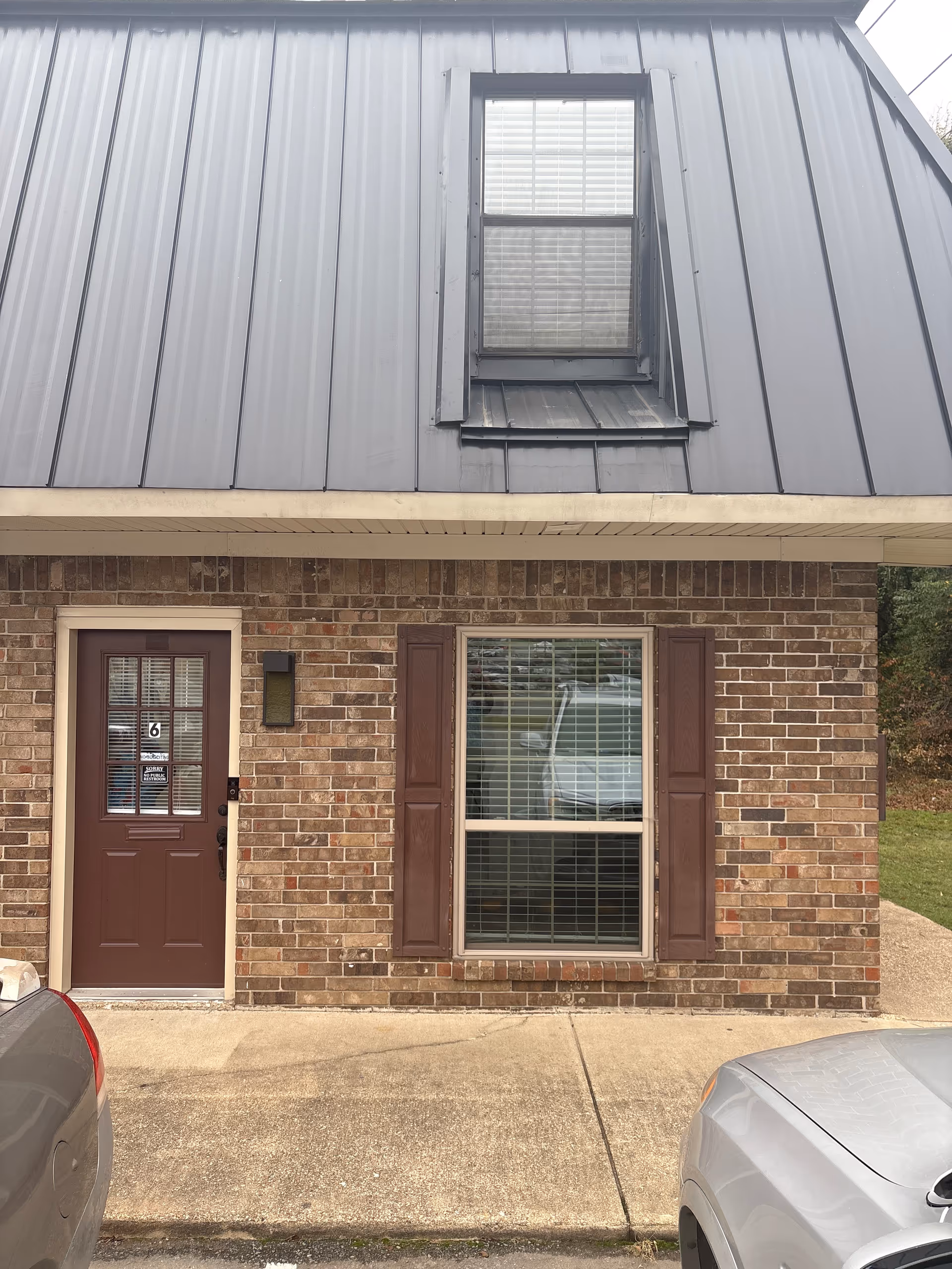 Exterior view of a brick building front with a brown door and window shutters.