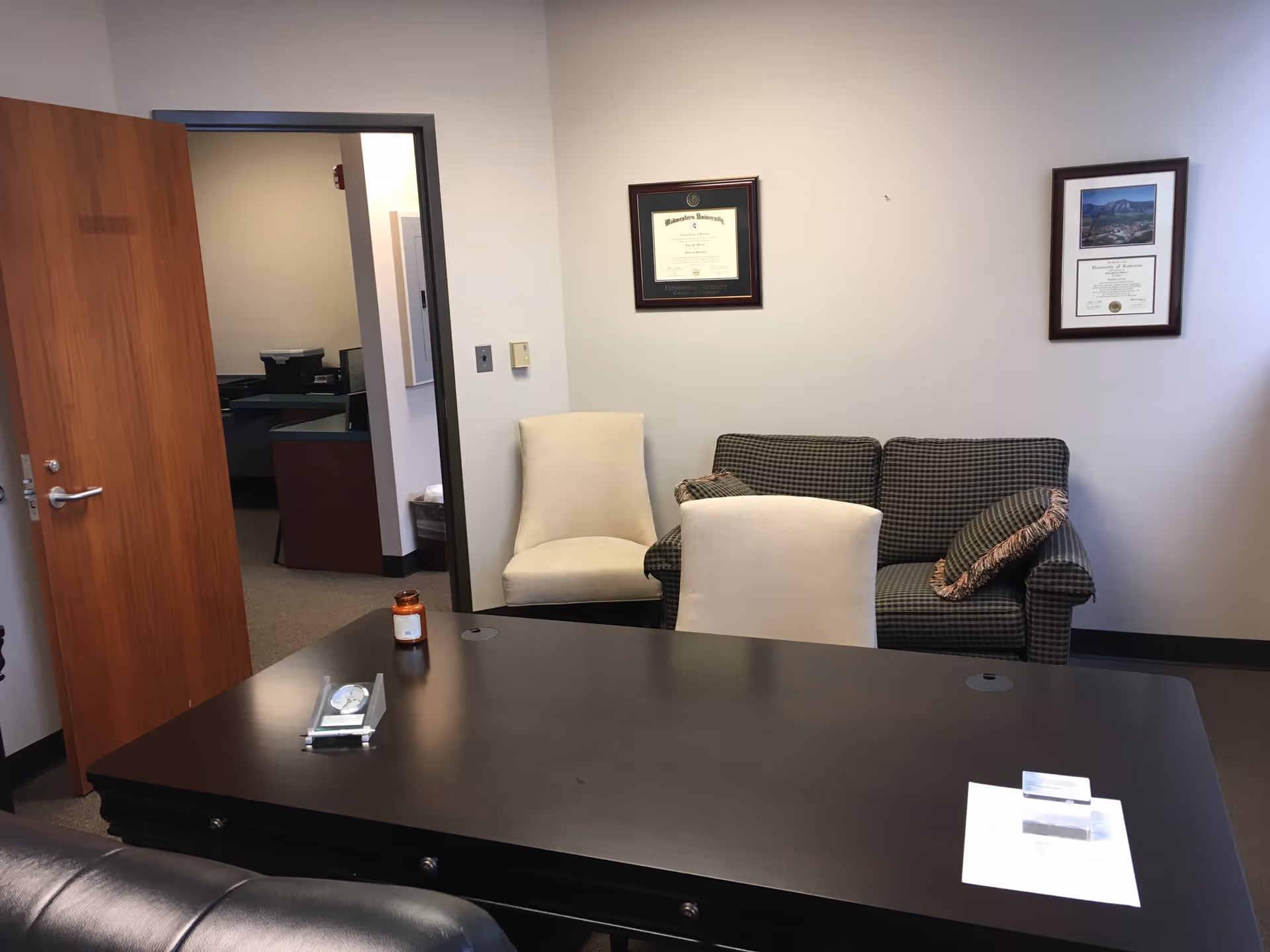 Office conference area in a clinic with a large desk, couch, and framed certificates.
