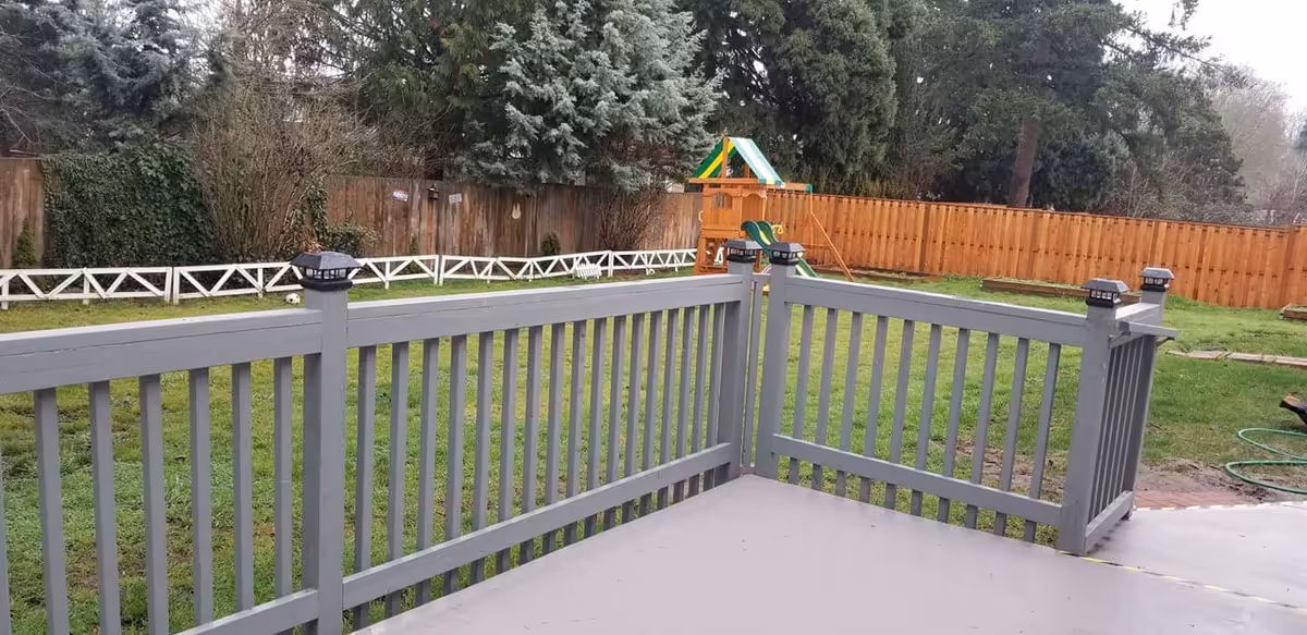 Gray wooden deck railing overlooks a grassy yard with a children's playset and fence.