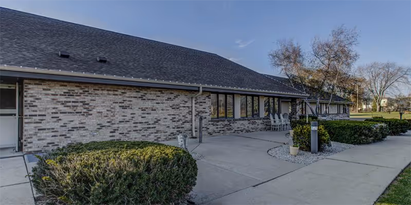 Exterior view of Elizabeth Residence Oak Creek with brick walls, shrubs, and outdoor seating.
