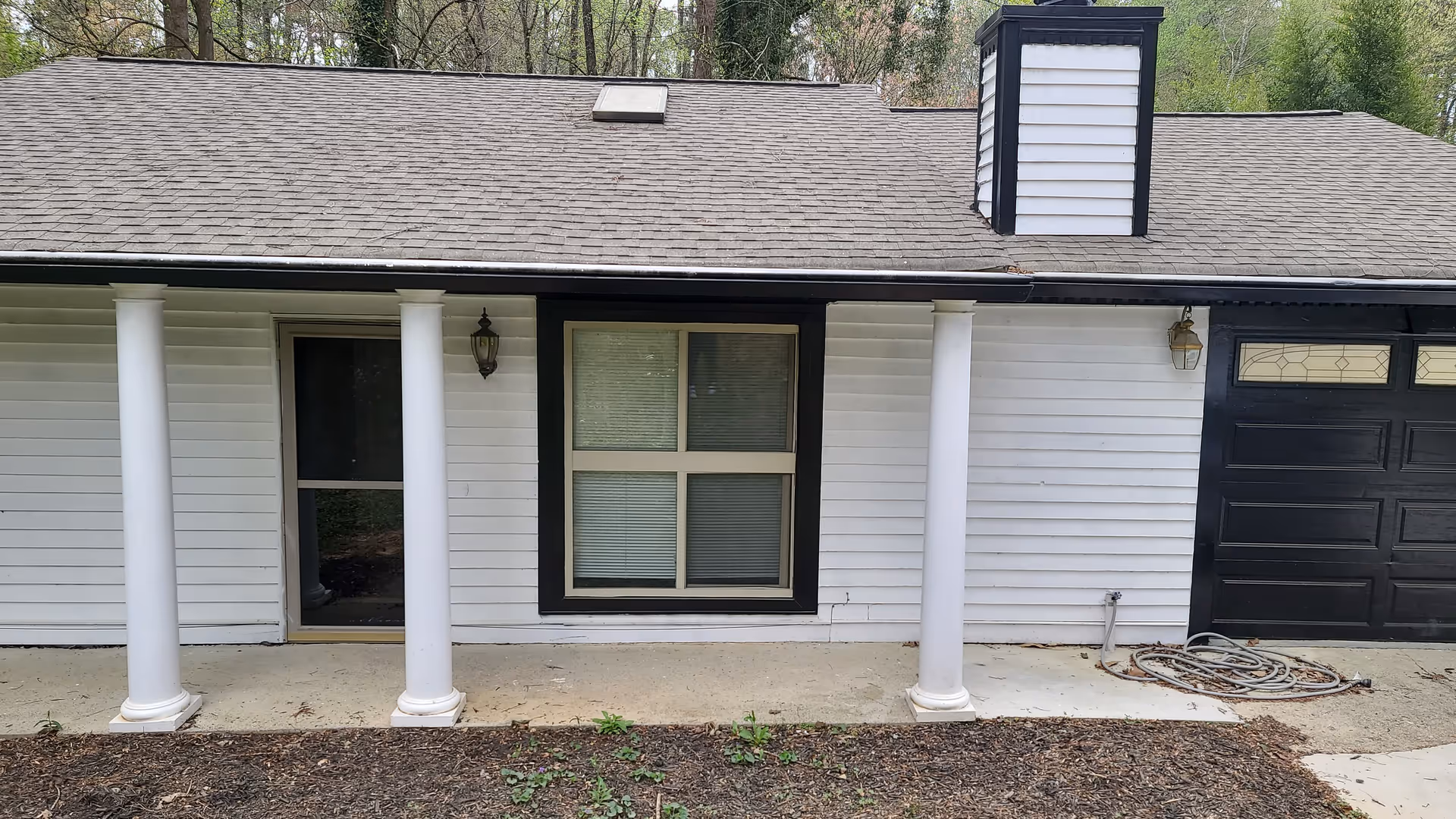White single-story building with columns, front door, window, and black garage door
