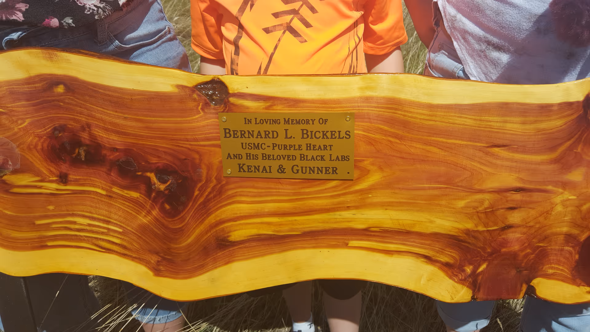 Close-up of a wooden memorial bench plaque outdoors with engraved dedication.