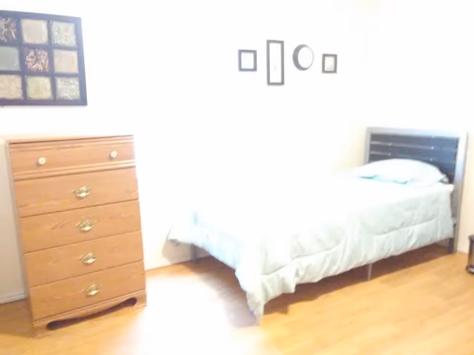 A simple bedroom with a twin bed, wood dresser, and wall decorations.