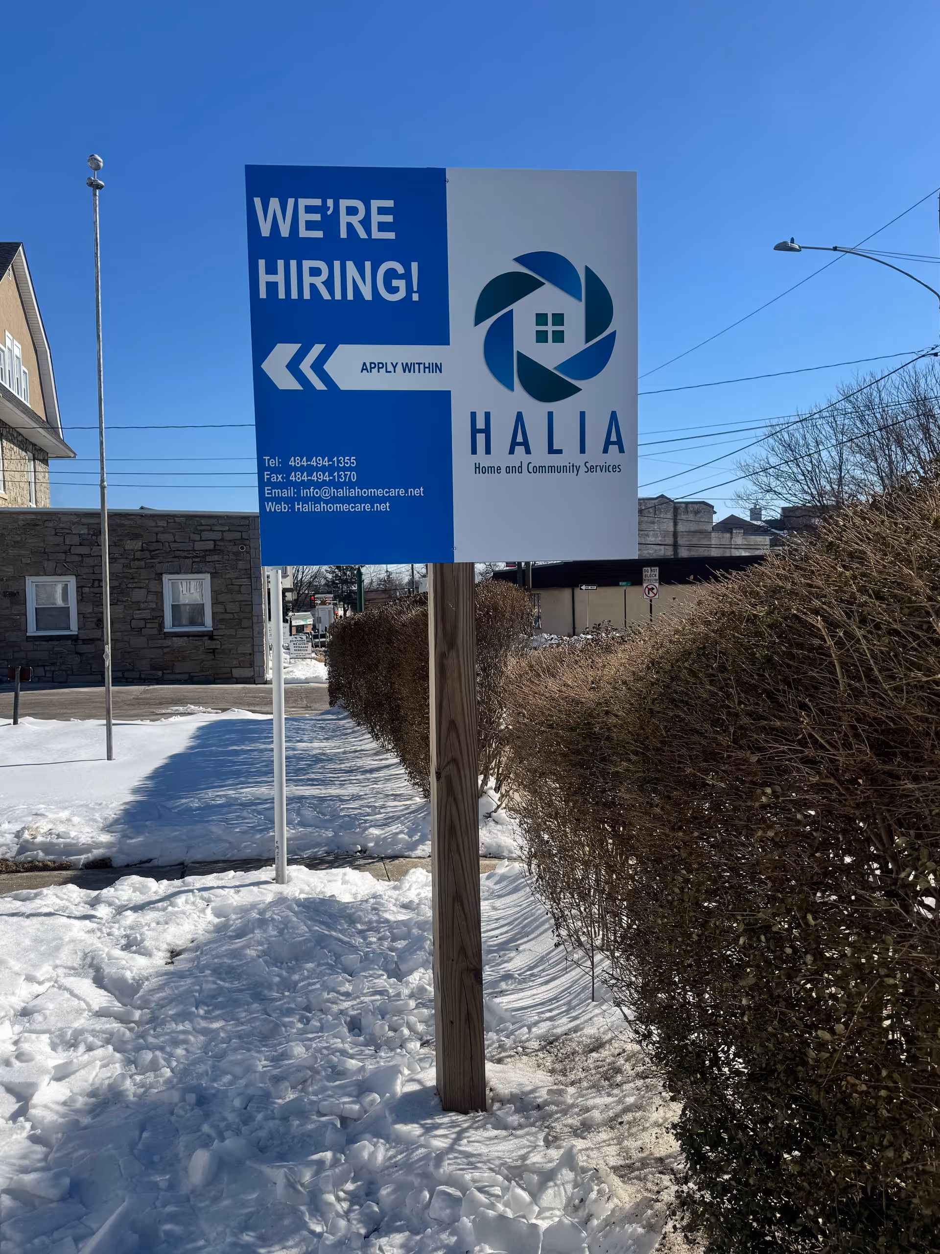 Blue and white Halia sign reading 'WE'RE HIRING!' outside a snowy facility.