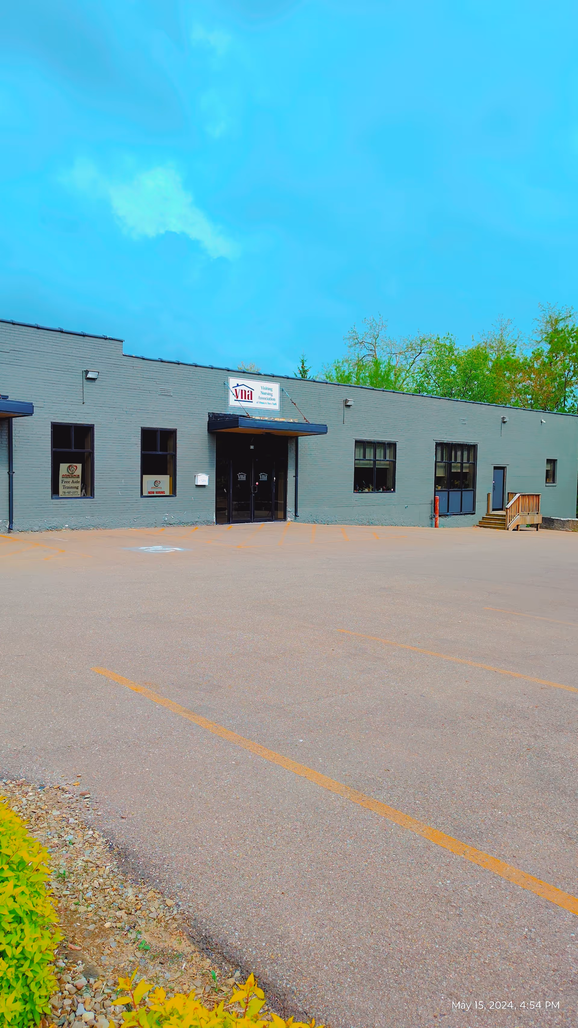 Front exterior of a gray facility with entrance and a parking lot.