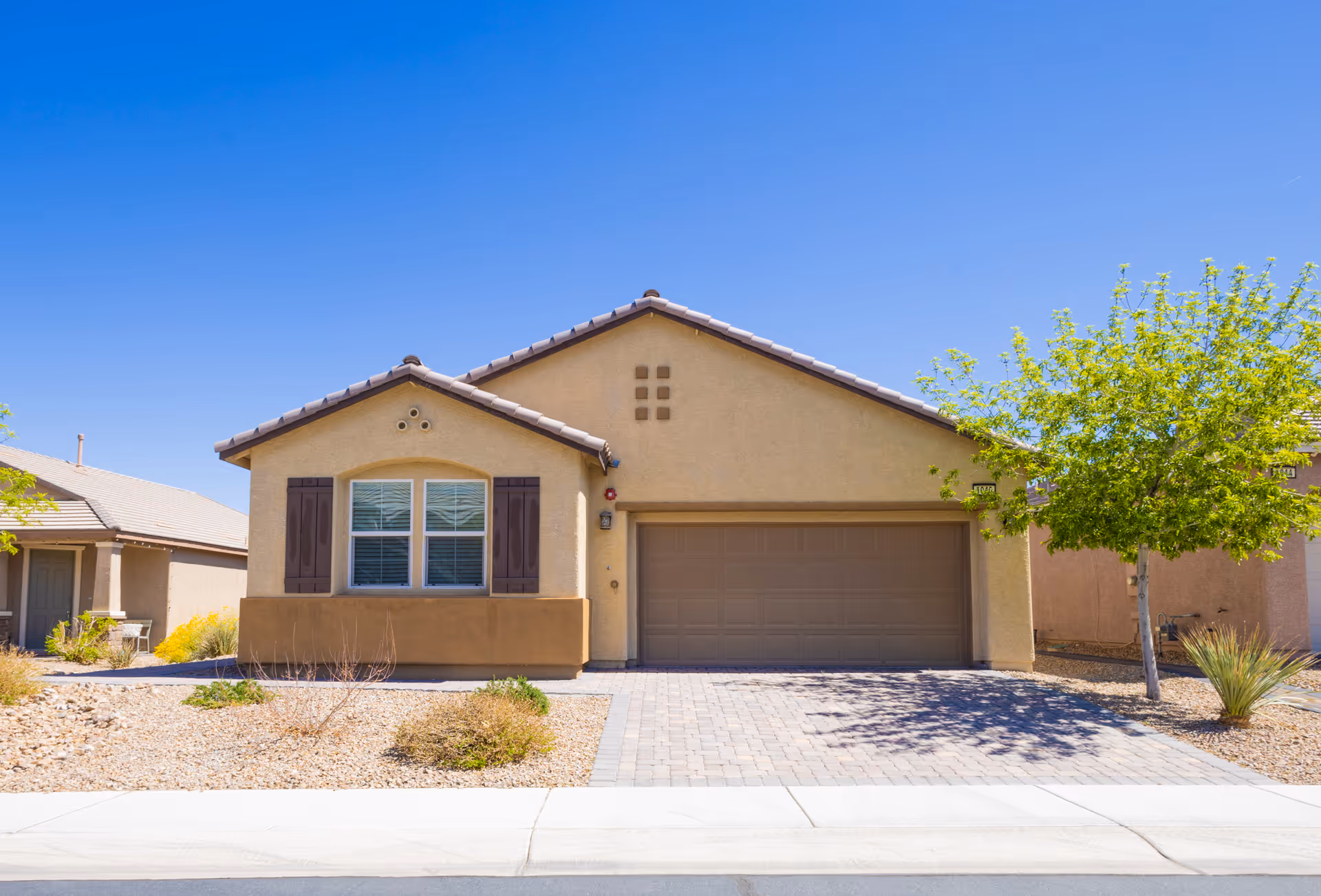 Front exterior of a single-story beige house with a two-car garage and desert landscaping.