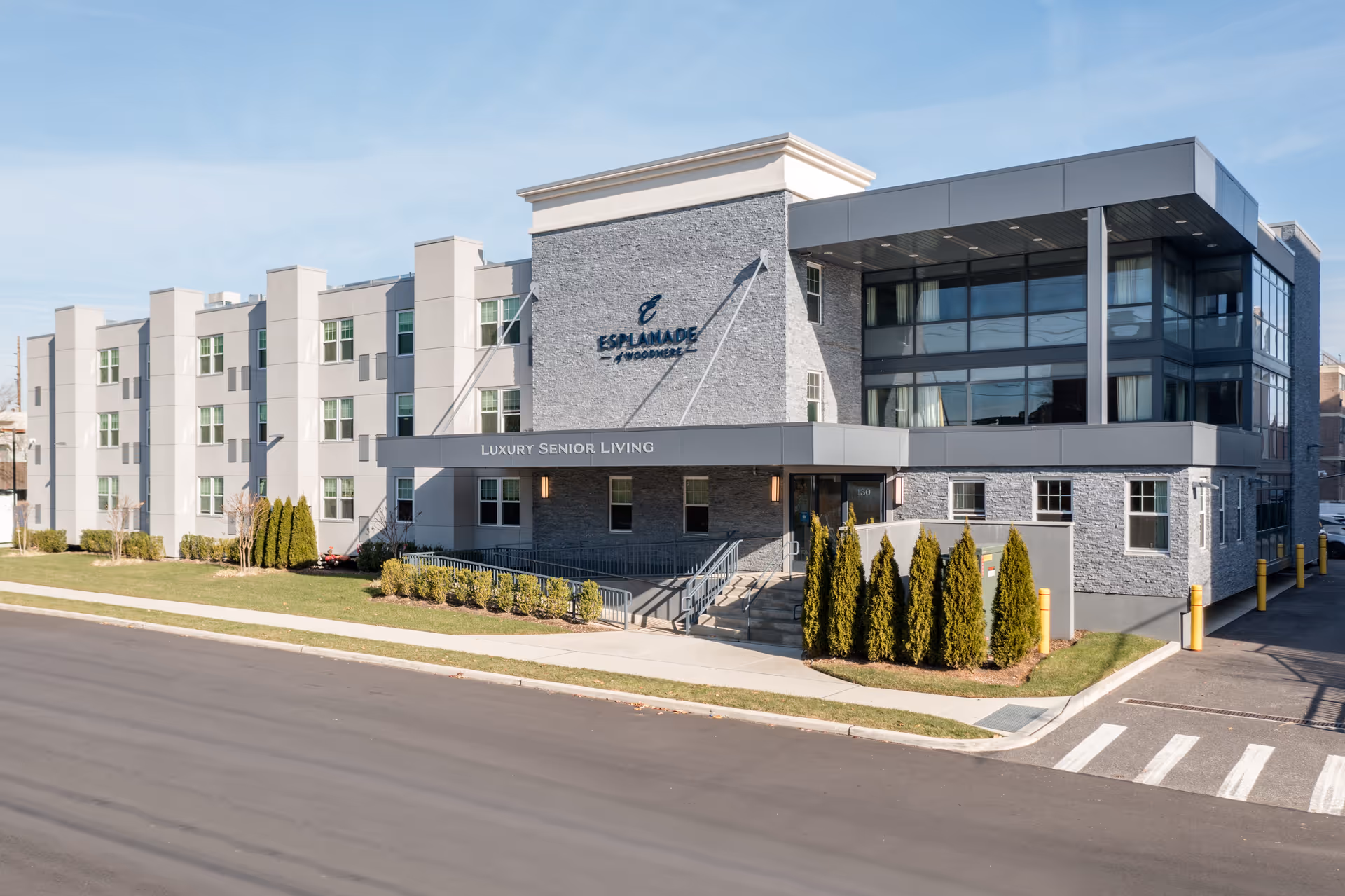 Exterior view of Esplanade of Woodmere luxury senior living facility with entrance and landscaping.