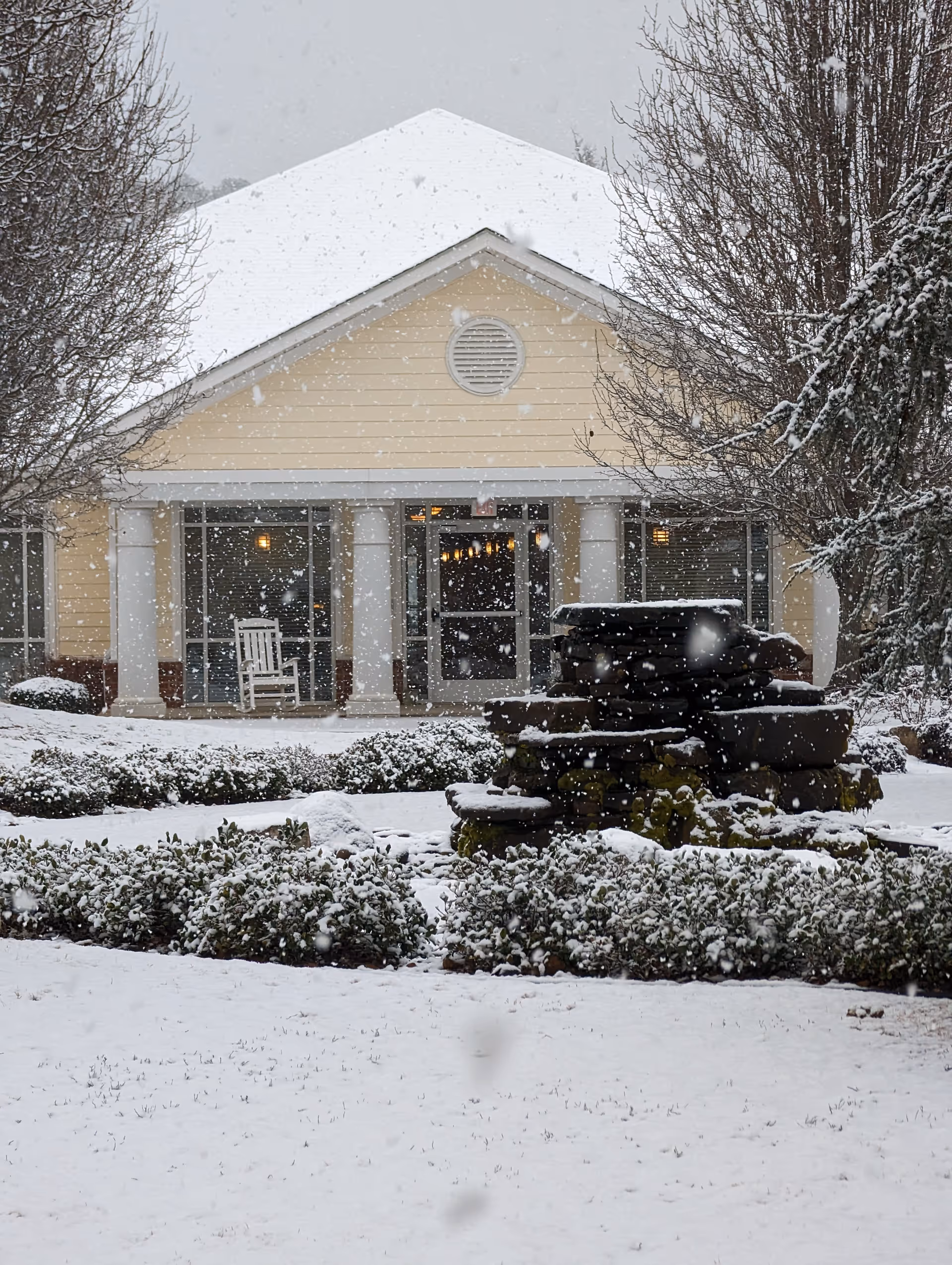 Snowy front entrance of Mt. Carmel Community at the Village with a stone fountain.