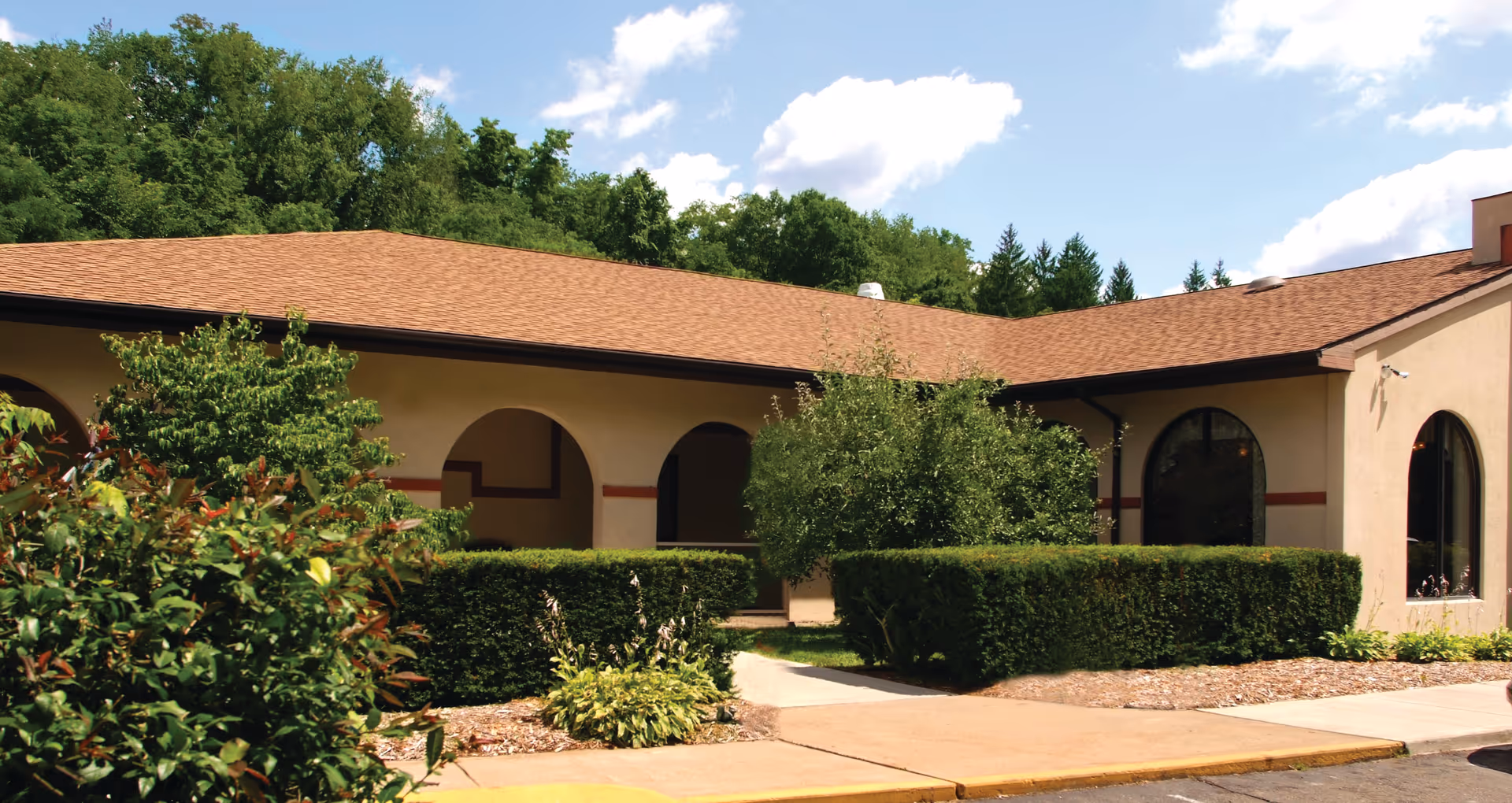 Single-story facility with arched entrances, hedges, and a sidewalk courtyard.
