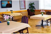 A bright dining room with beige tablecloths, flowers, and empty chairs.