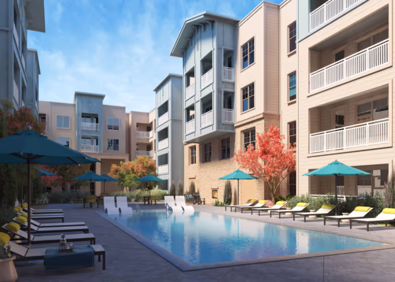 Outdoor courtyard of a senior living facility with a pool, lounge chairs, and umbrellas.