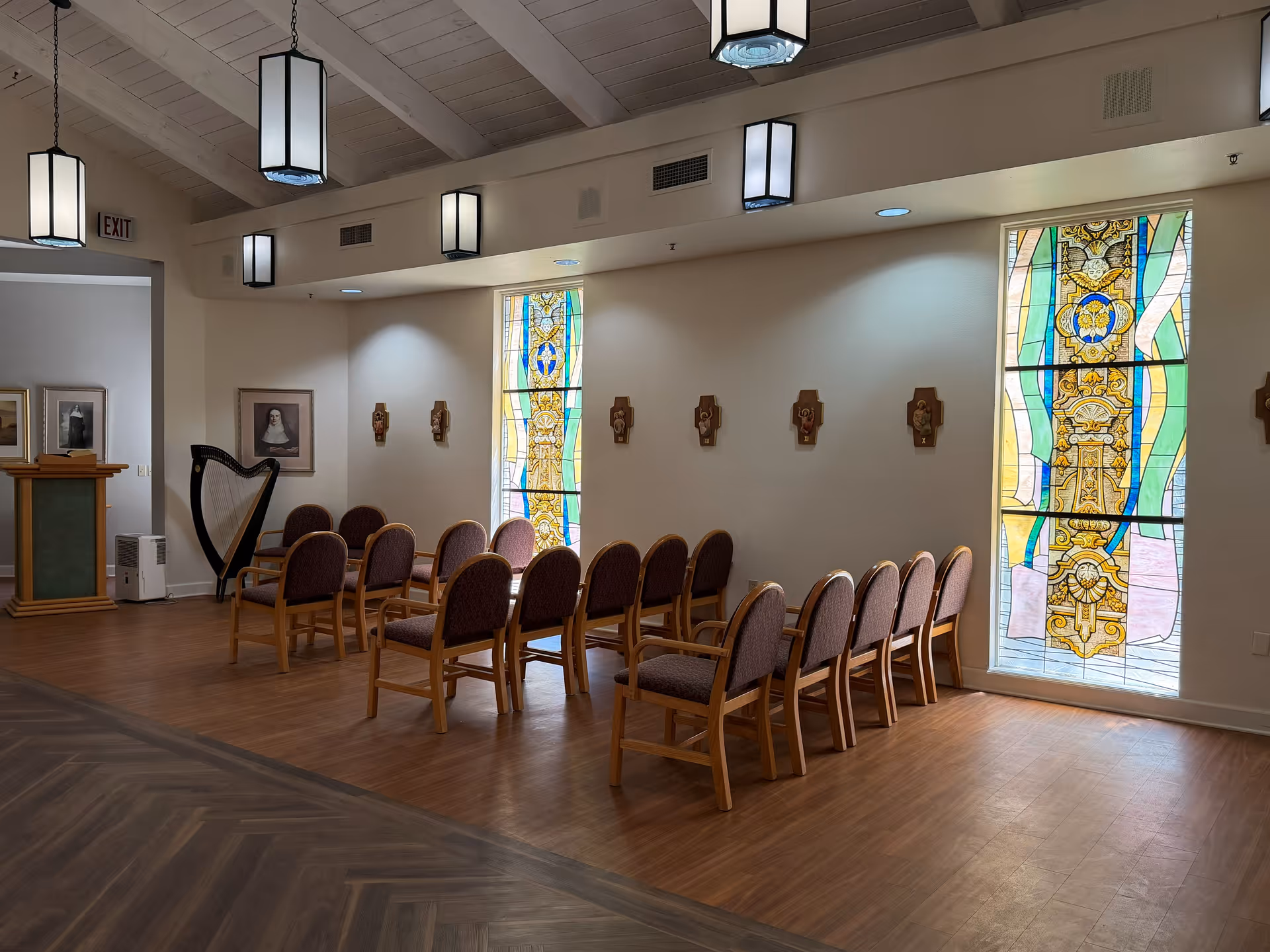 Chapel-like interior with wooden chairs arranged in rows, stained glass windows, and a harp.