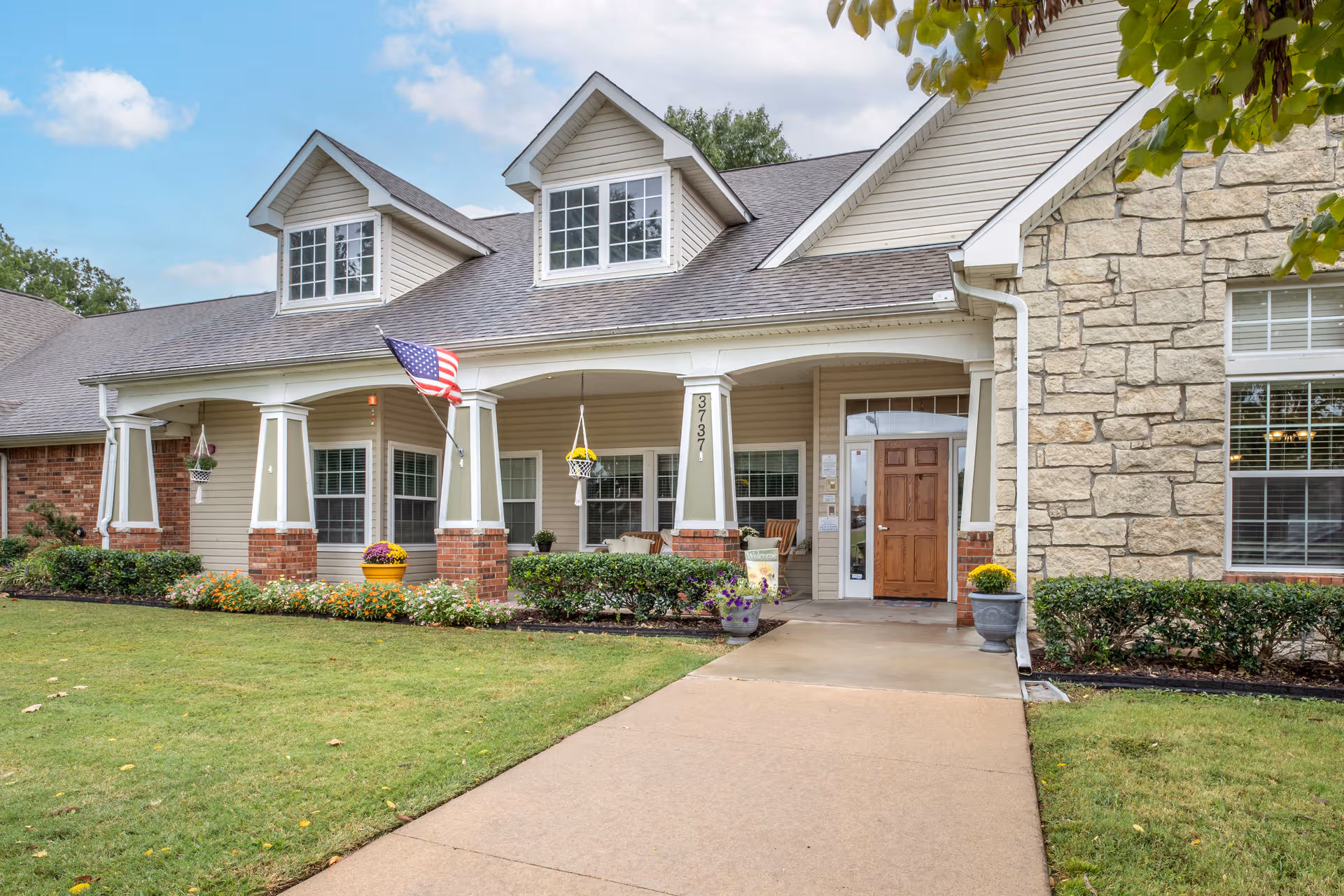 Front entrance of a senior living facility with porch, flag, and landscaping.