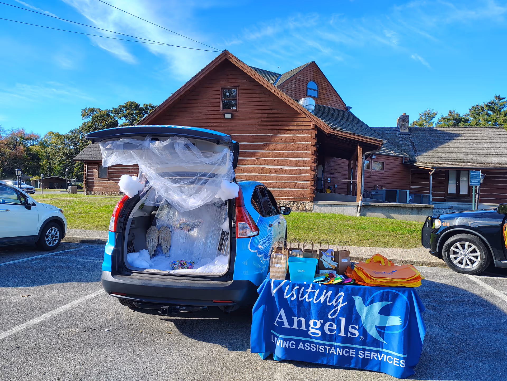Blue van with open trunk and display table outside a Visiting Angels facility.