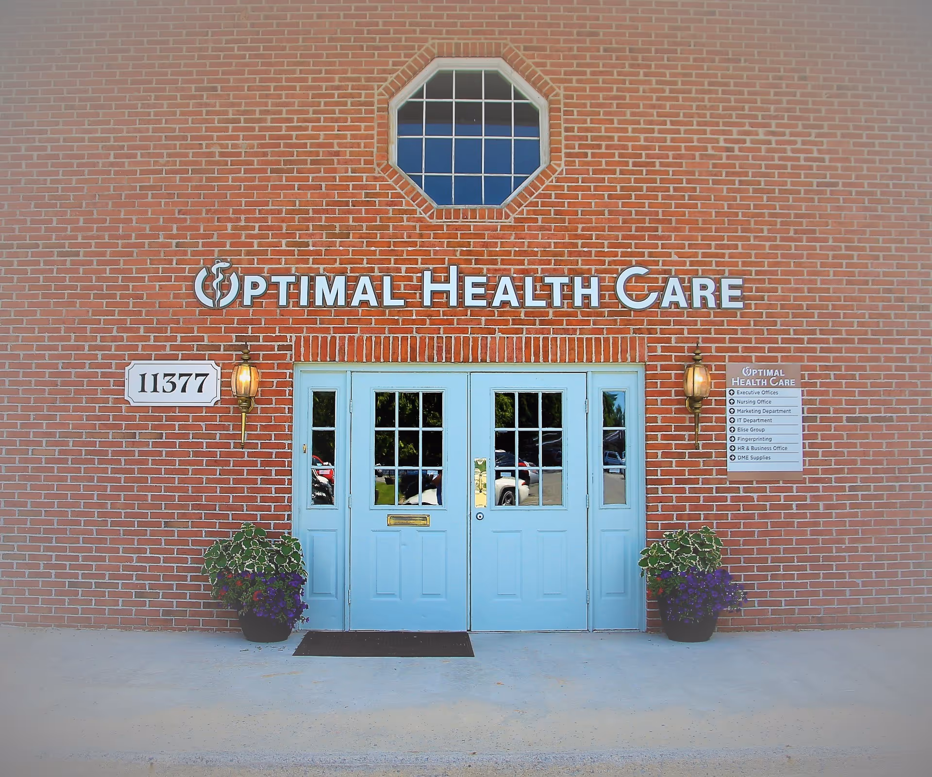 Brick building entrance with blue double doors and Optimal Health Care sign