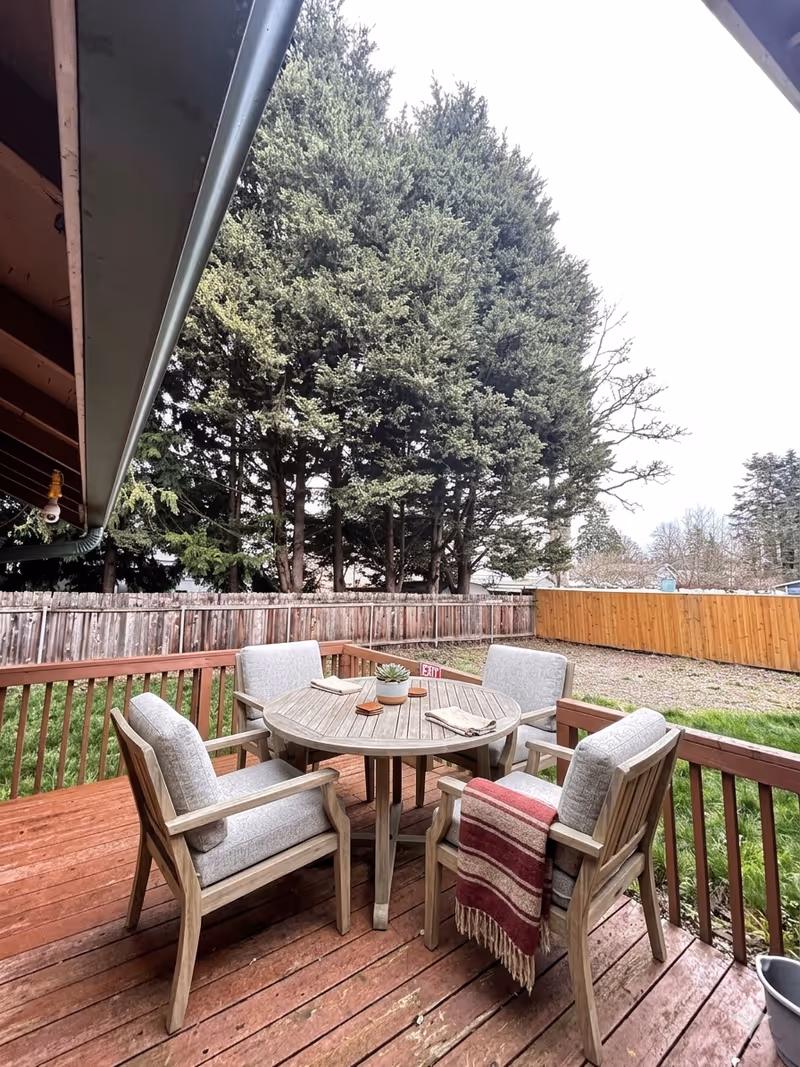 Outdoor wooden deck with a round table, cushioned chairs, and a blanket.