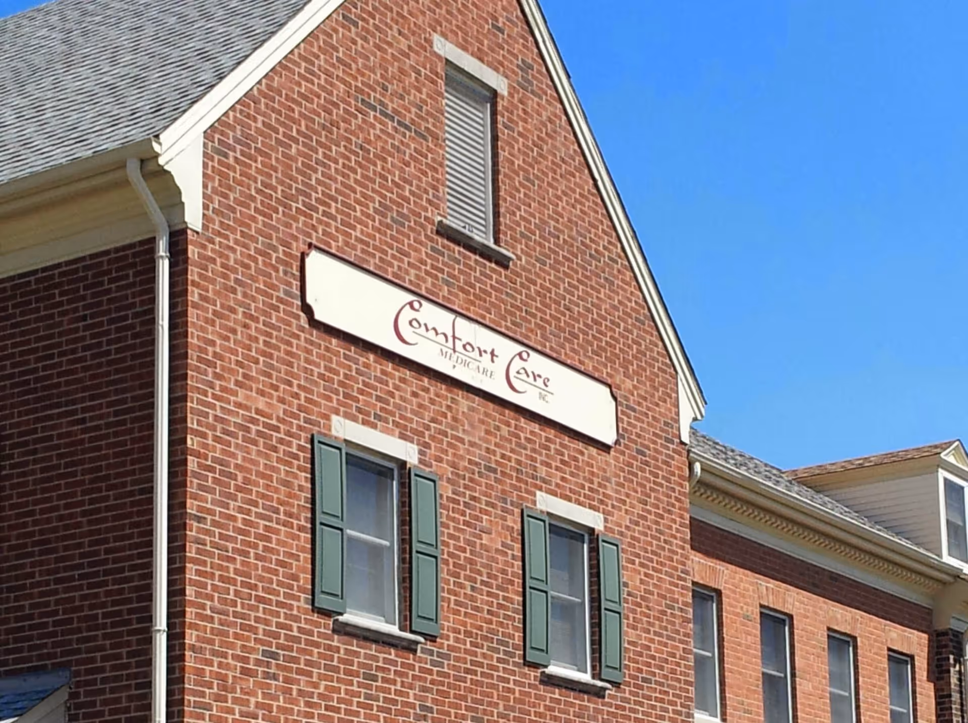 Exterior brick building of Comfort Care Medicare with sign and green shutters.