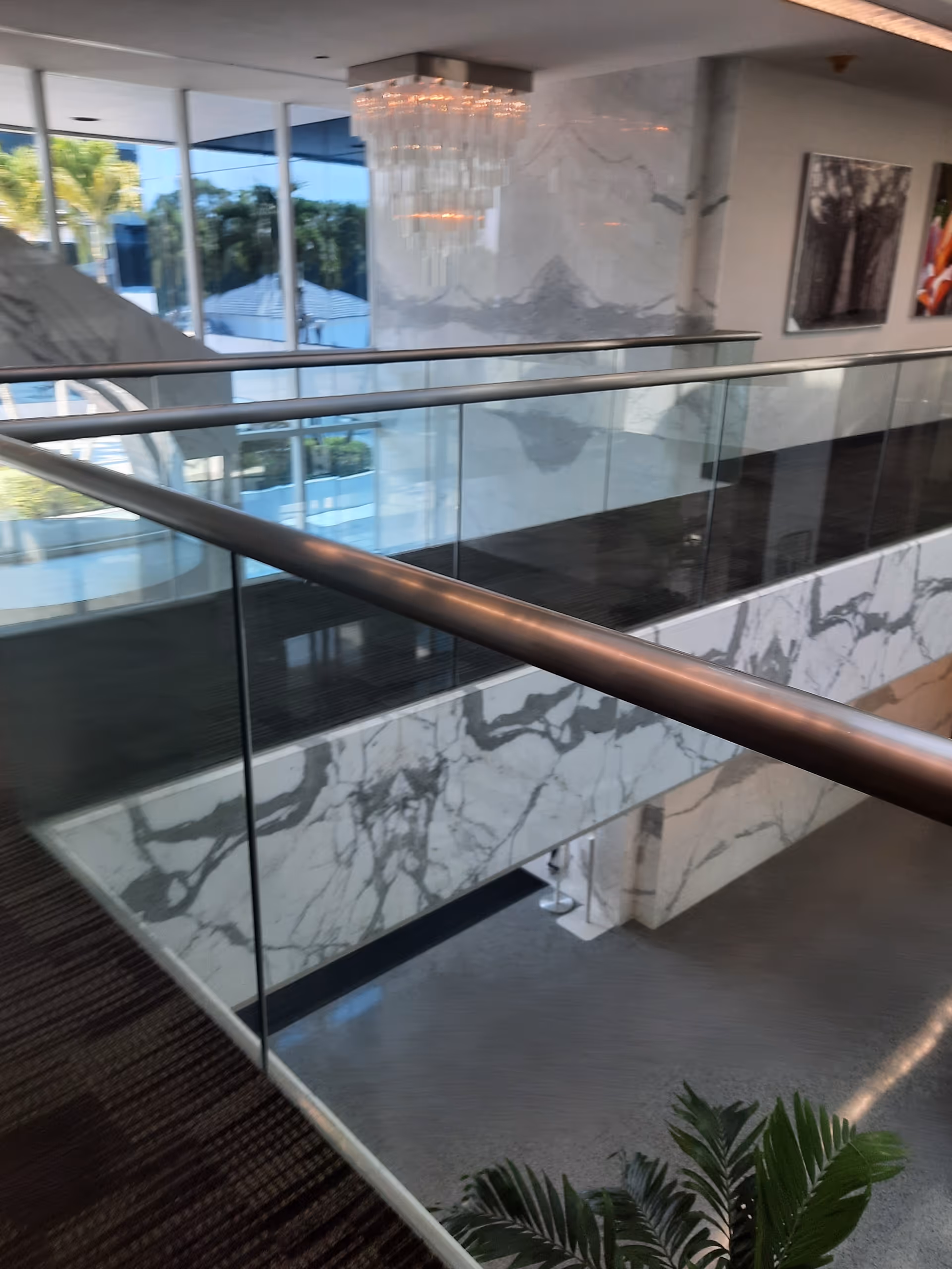 Luxurious interior with glass railing, marble walls, chandelier, and framed artwork.