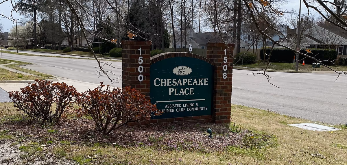 Brick entrance sign reading "Chesapeake Place" with address numbers 1500 and 1508 beside a road and low shrubs.