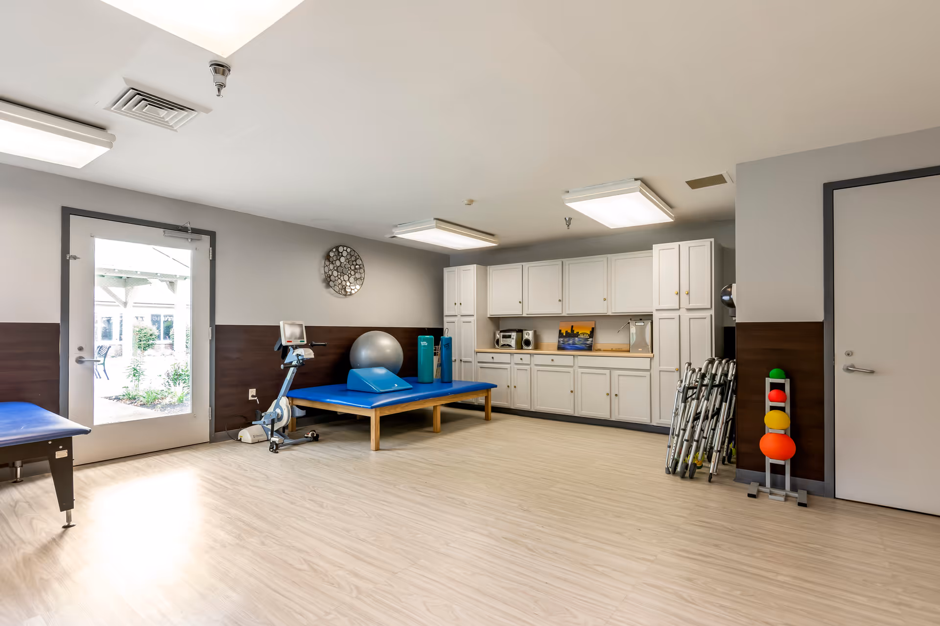 Interior rehab room with exercise equipment, therapy table, and white cabinets.
