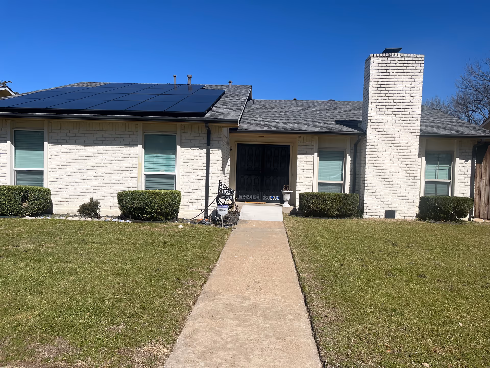 Single-story white brick care home with front entrance, shrubs, and solar panels.