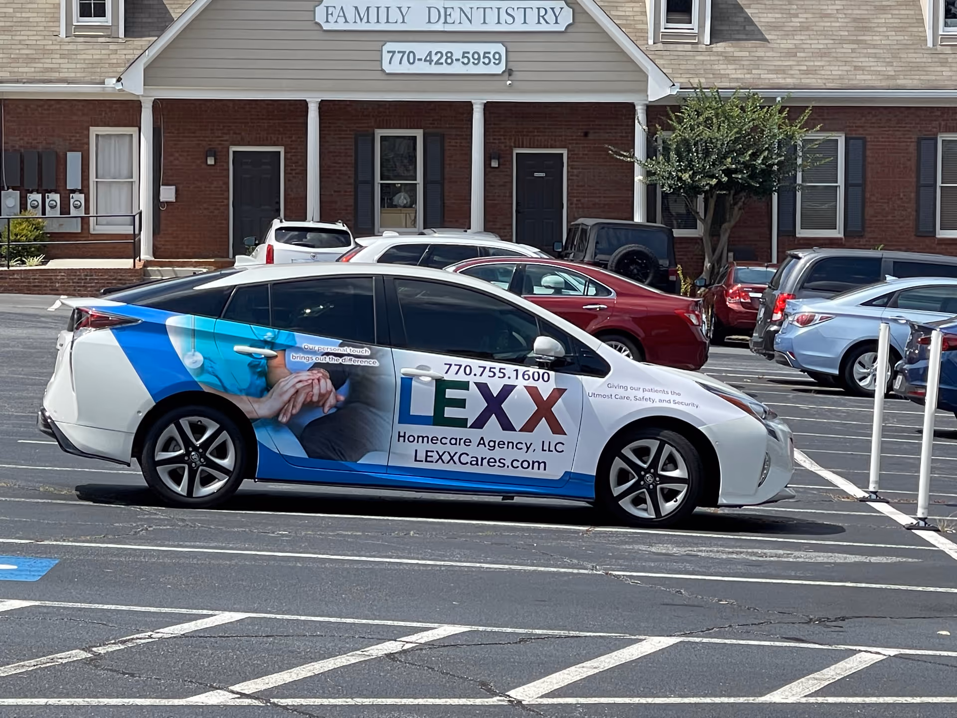 Branded LEXX Homecare Agency car parked in a lot near a brick building with dentistry sign