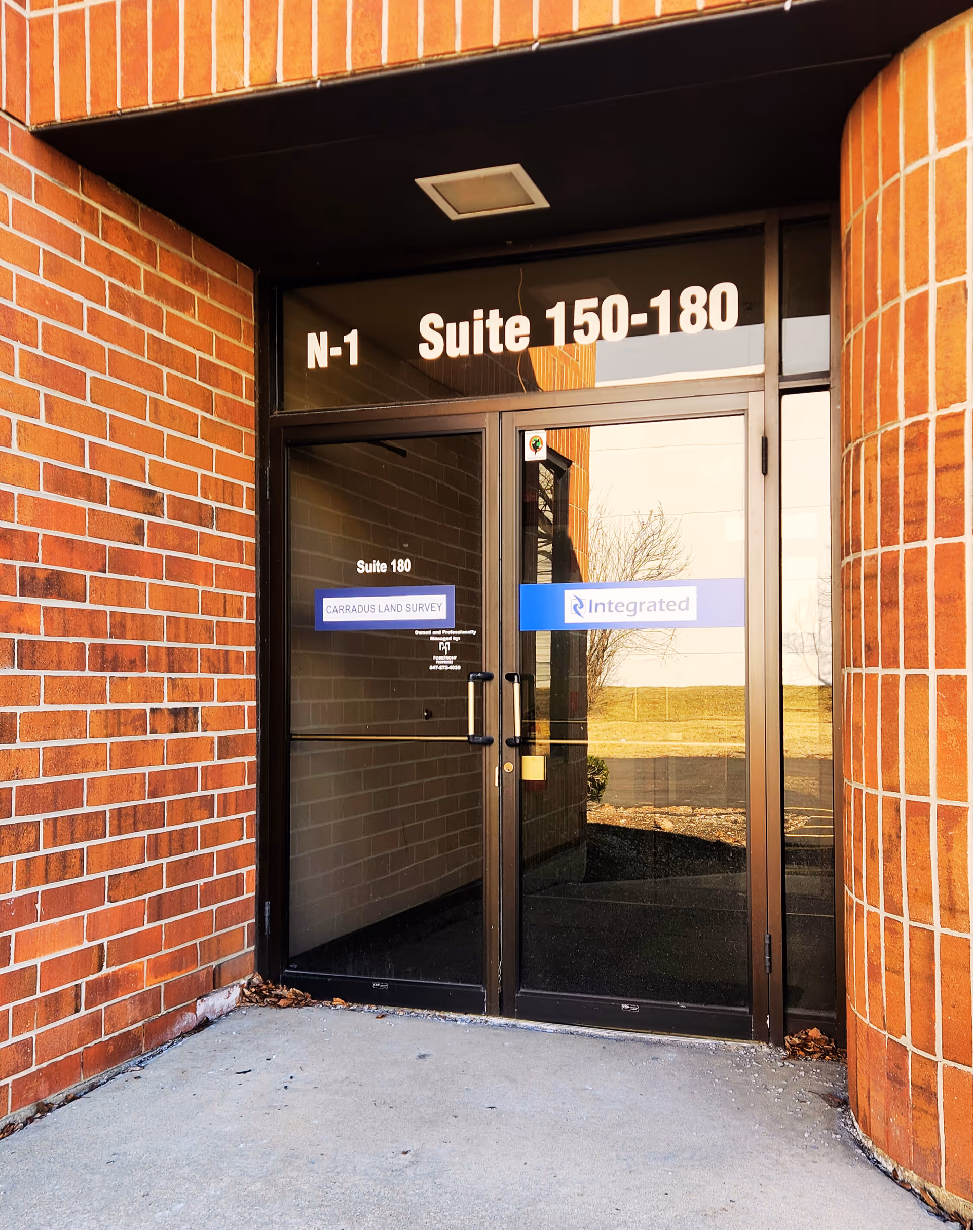 Exterior view of a brick building entrance with glass doors and suite numbers.