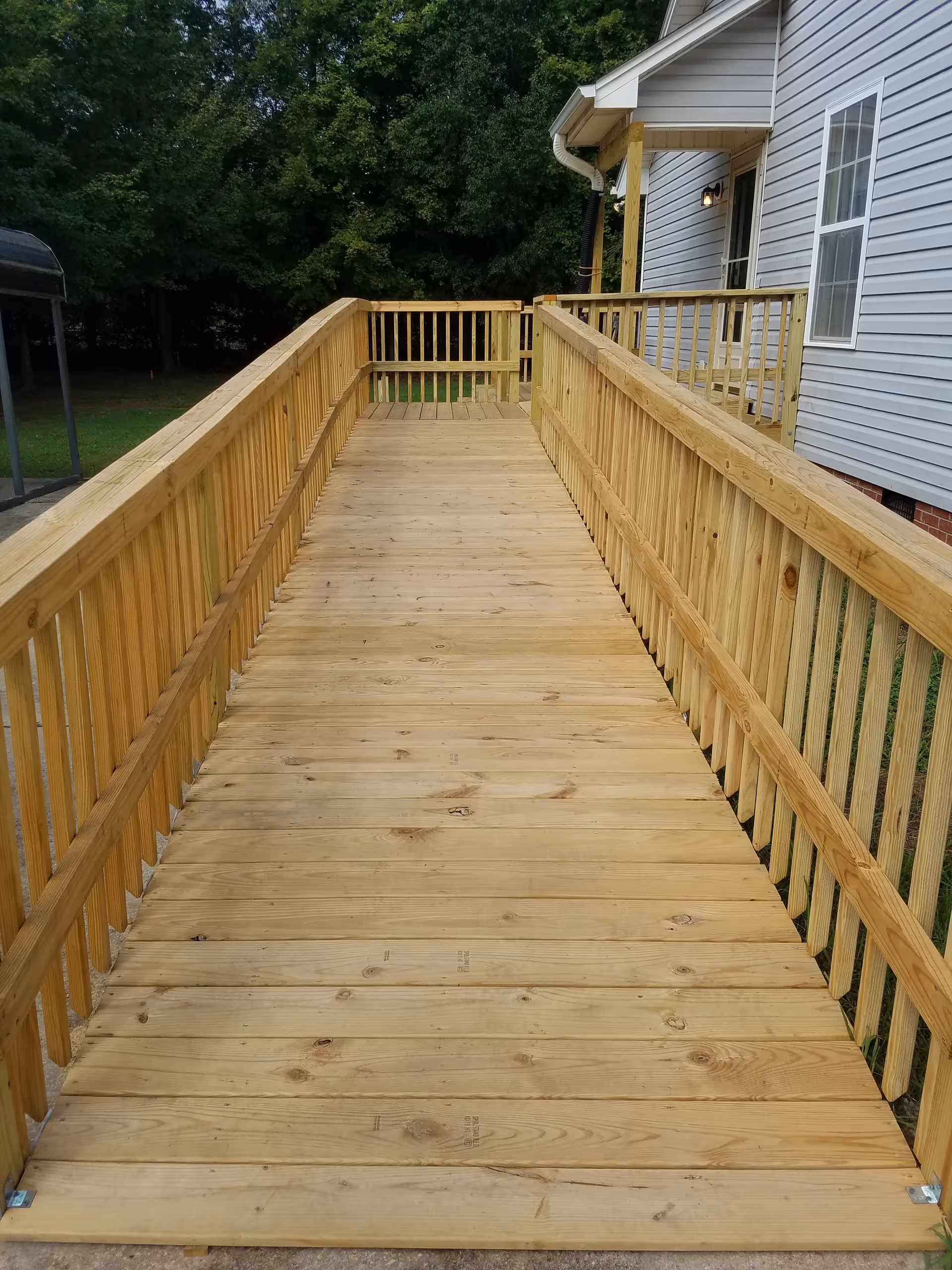 Long wooden outdoor ramp with railings leads to a house entrance.