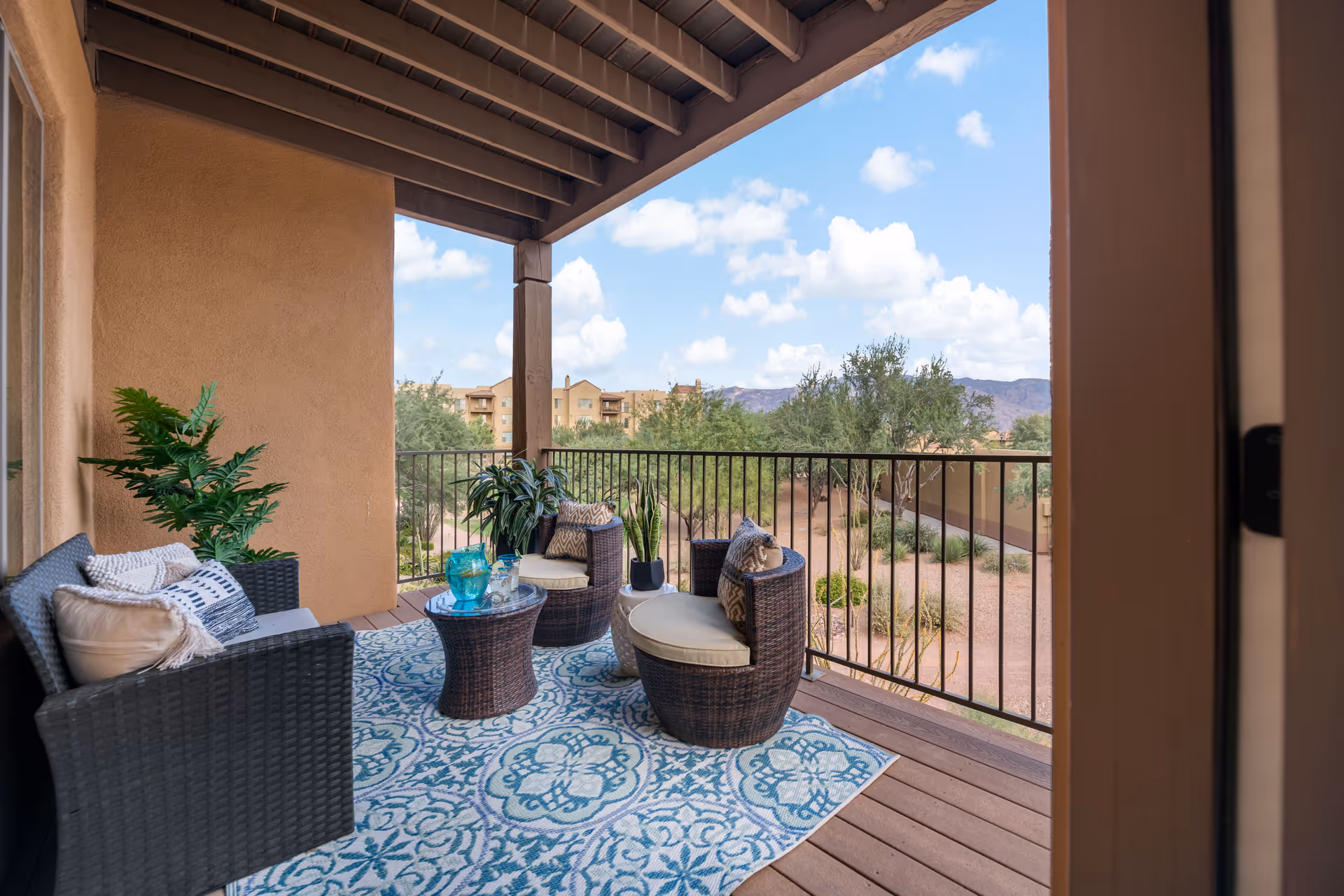 Outdoor balcony with wicker seating, rug, and potted plants; desert landscape beyond.