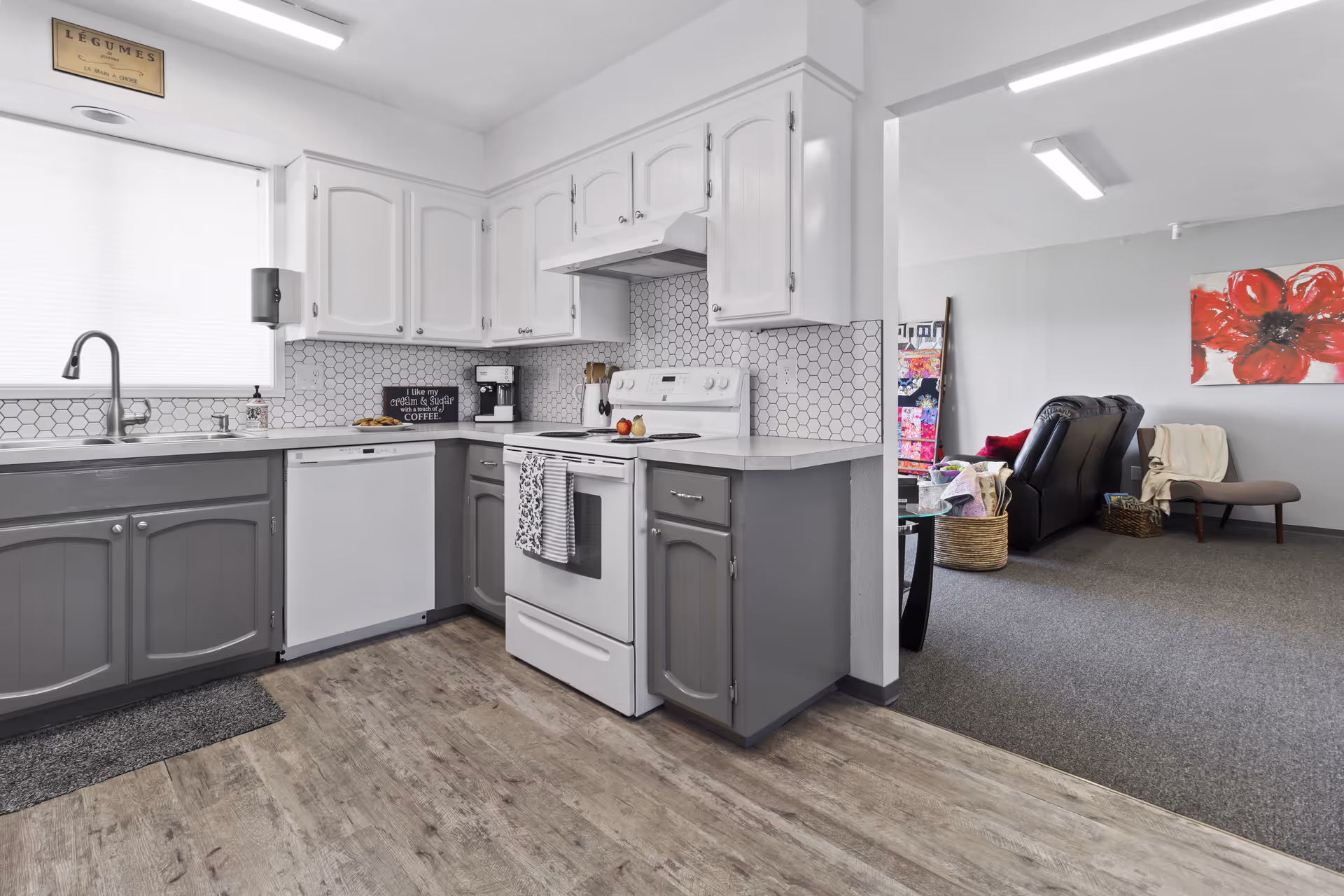 Kitchen with white upper cabinets, gray lower cabinets, hex backsplash, stove, dishwasher, and open living area.