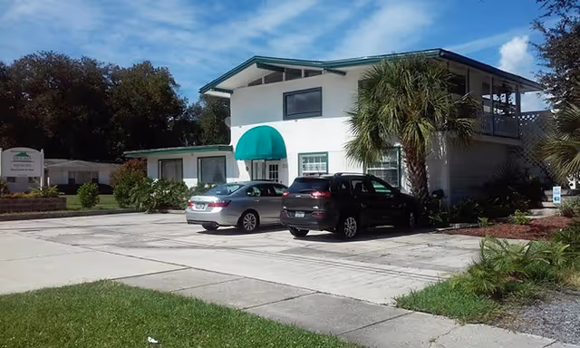 Exterior view of a two-story senior living facility with a green awning and cars.
