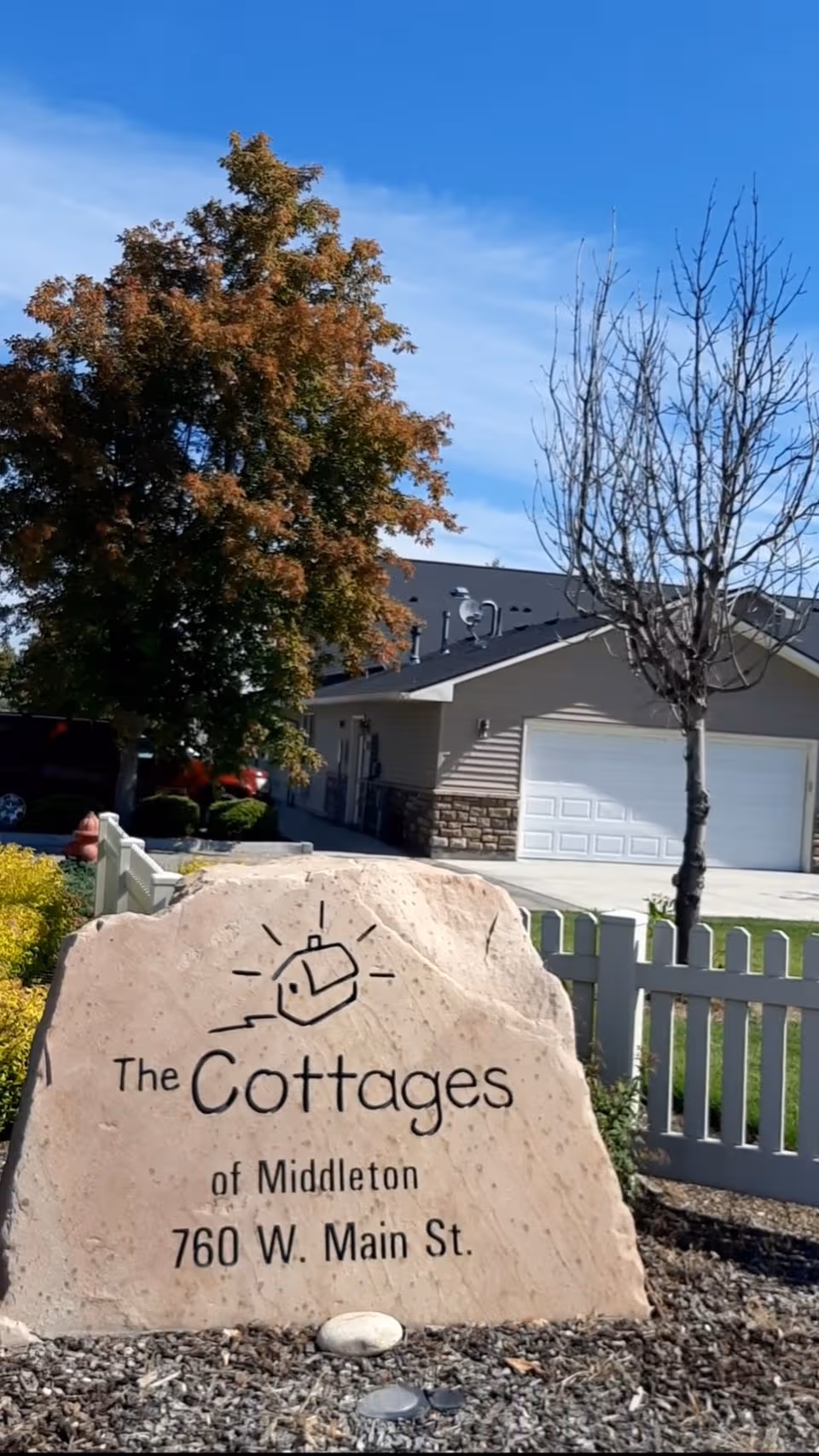 Front exterior view of The Cottages of Middleton with rock sign and white fence.