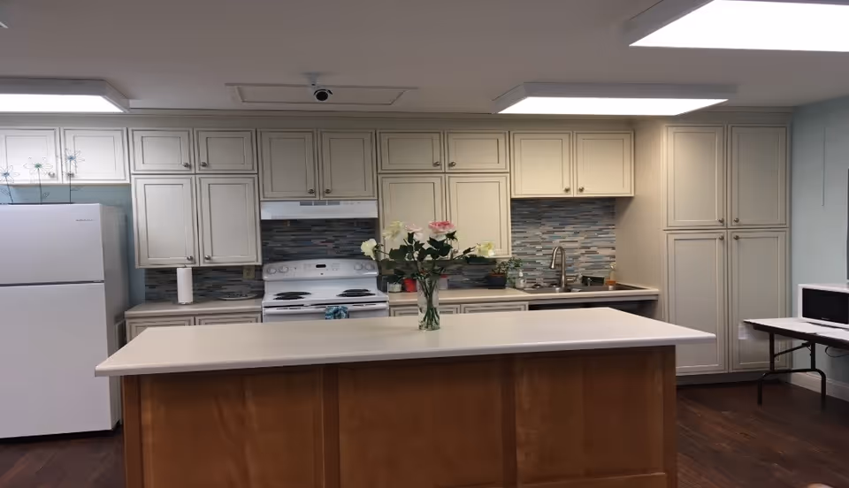 Bright kitchen with white cabinets, island, sink, and appliances in Lighthouse Manor.