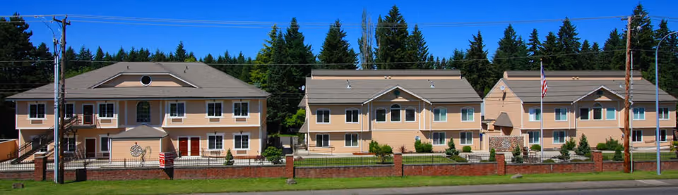 Row of beige senior living buildings with brick fence and green landscaping.