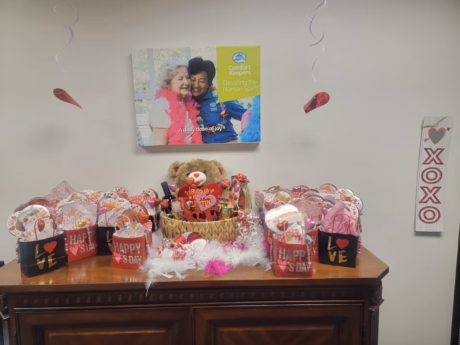 Valentine gift bags and a teddy basket arranged on a wooden cabinet in a decorated interior.