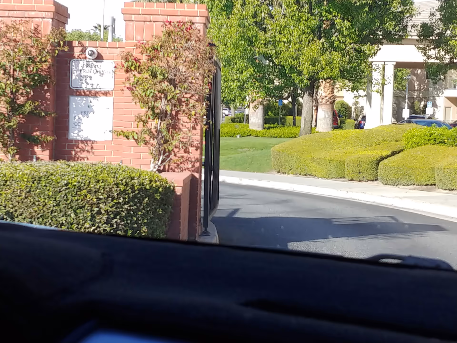 View of a gated entrance with brick pillars, trimmed hedges, and a driveway outside Riverwalk.