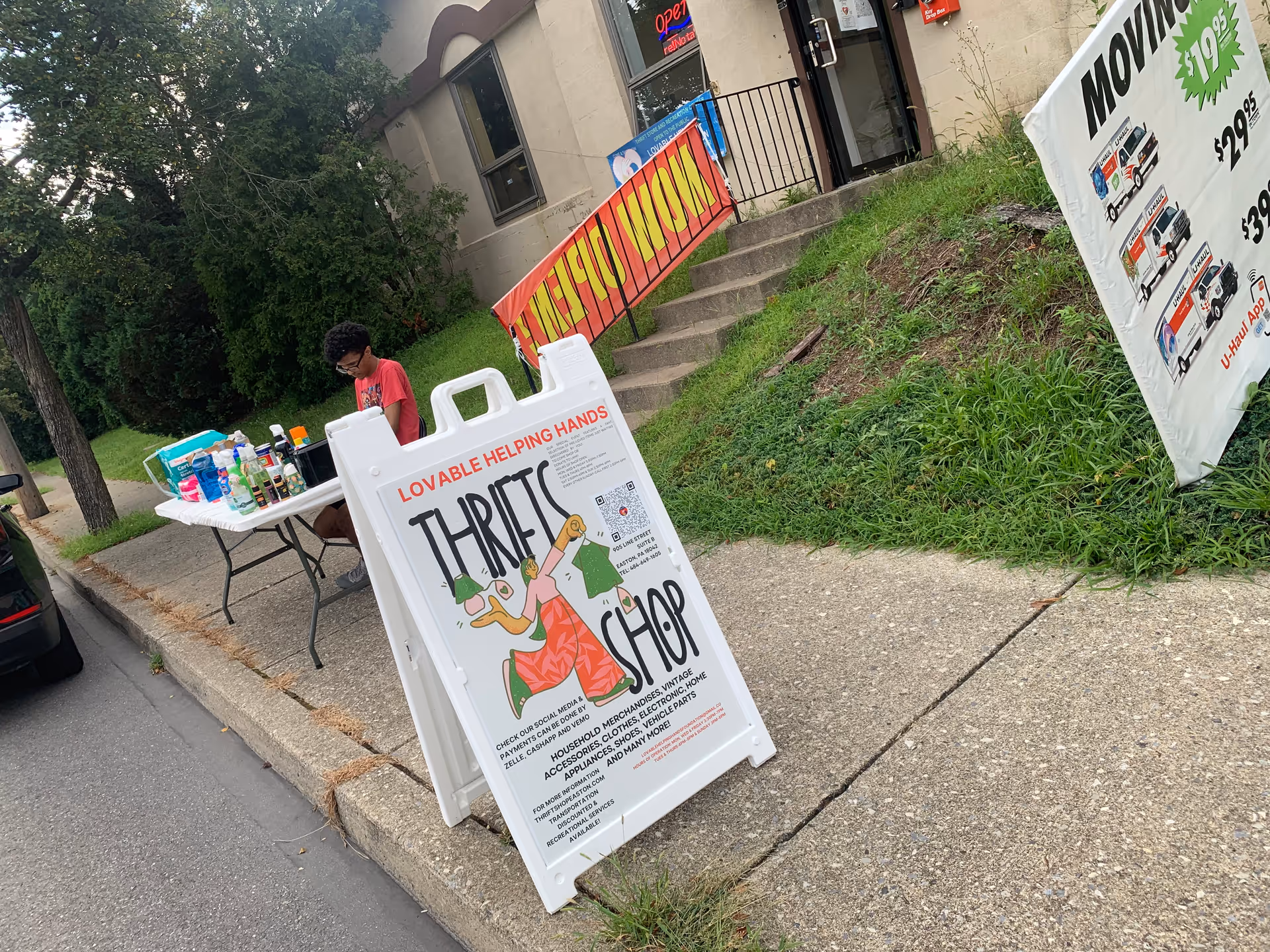 Outdoor thrift shop setup by Lovable Helping Hands Foundation; a person arranges items on a table.