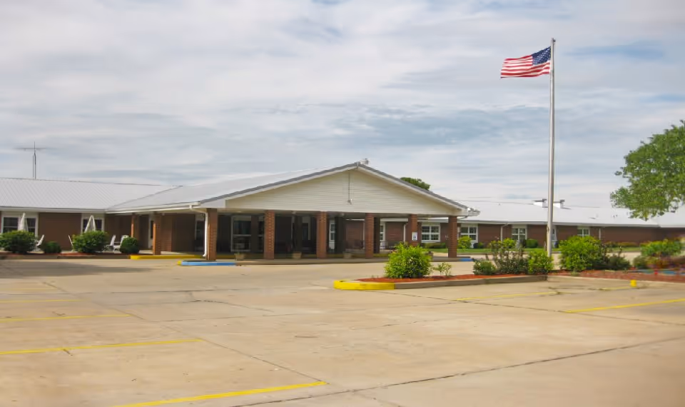 Single-story senior living facility with brick facade, American flag, and a parking lot in front.