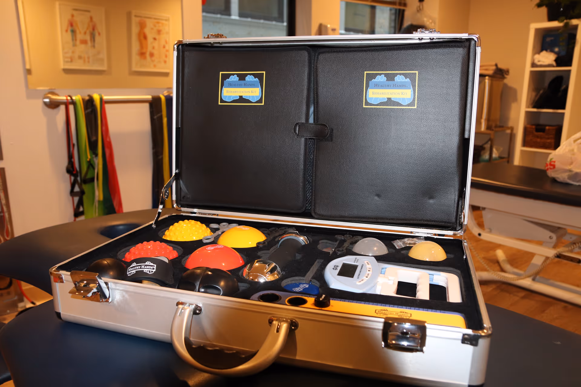Open silver case filled with colorful rehabilitation devices inside a clinic setting