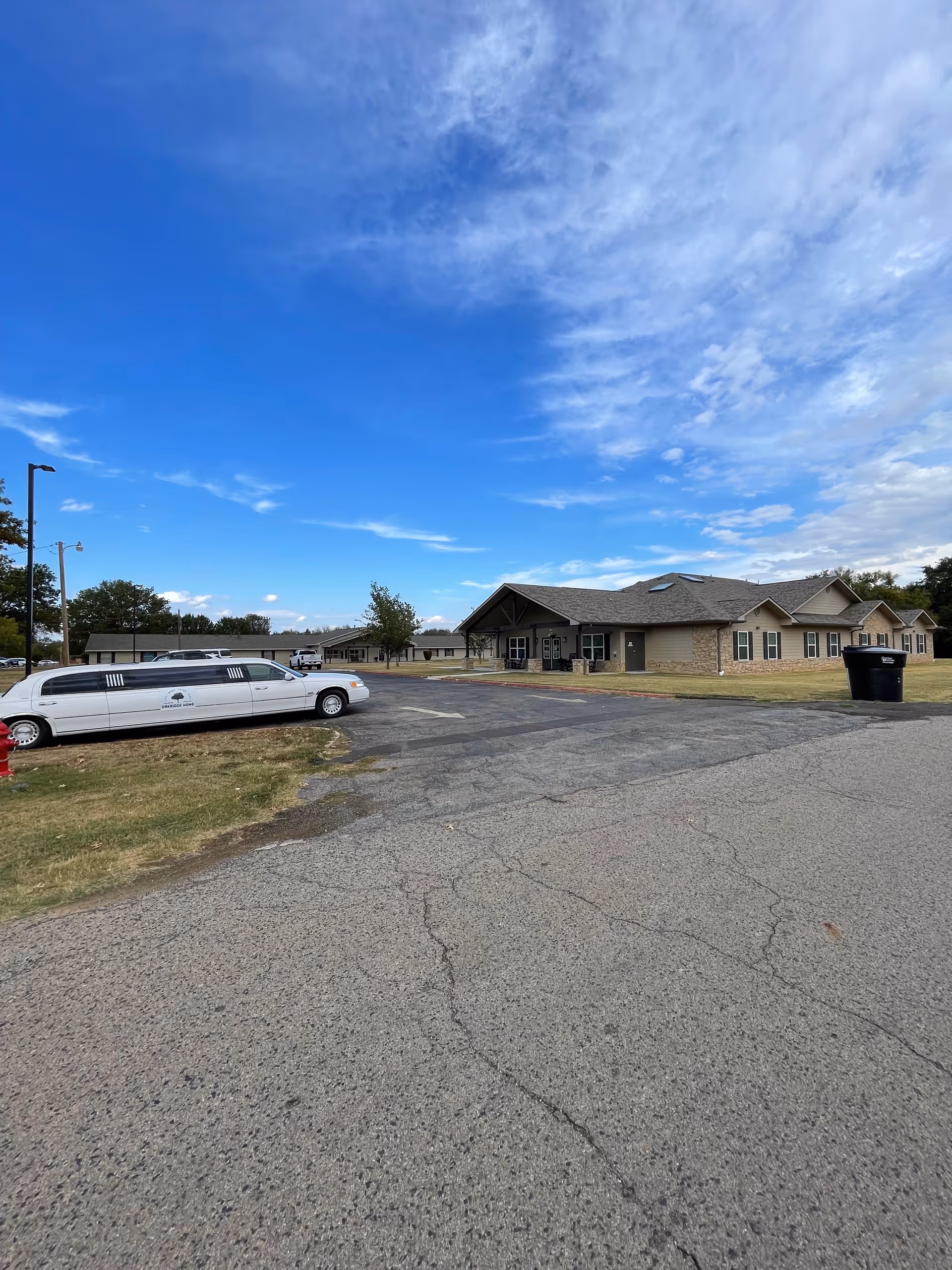 Exterior view of Oakridge Home facility with parking lot, limousine, and clear blue sky.