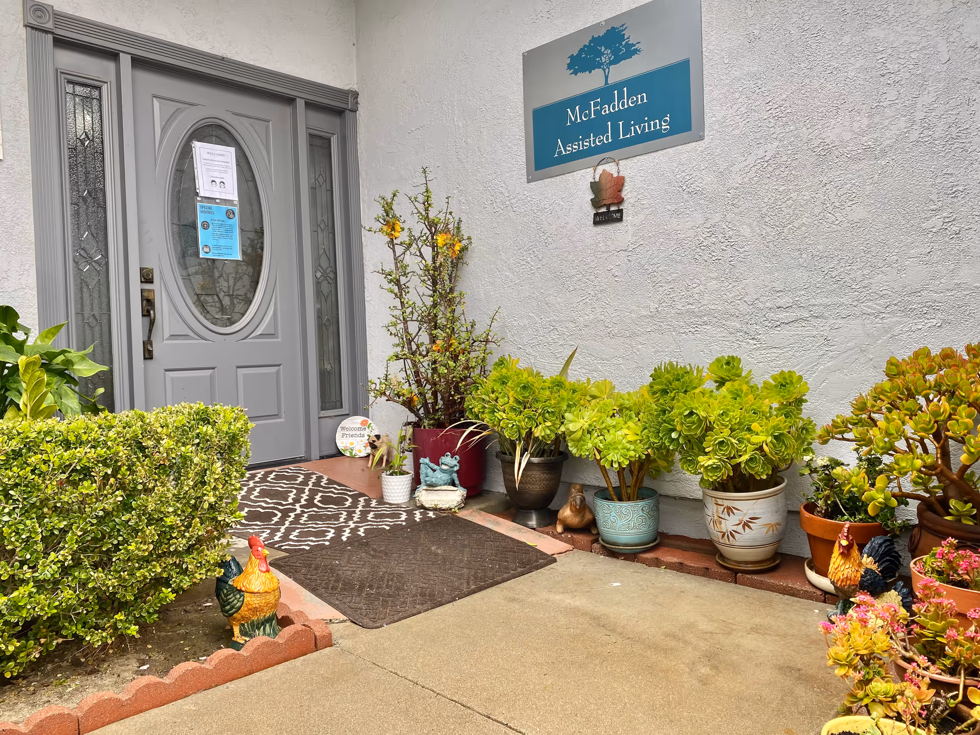 Front entrance of McFadden Assisted Living with potted plants along the doorway.