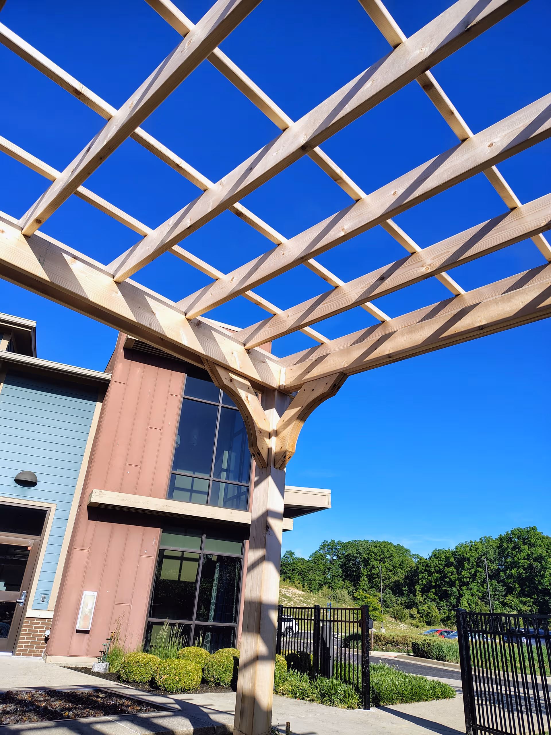 Wooden pergola frames the entrance of a modern building under a clear blue sky