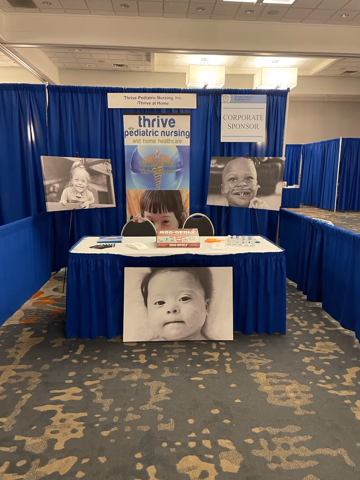 Blue exhibition booth with Thrive Pediatric Nursing banners and a table in a conference hall.