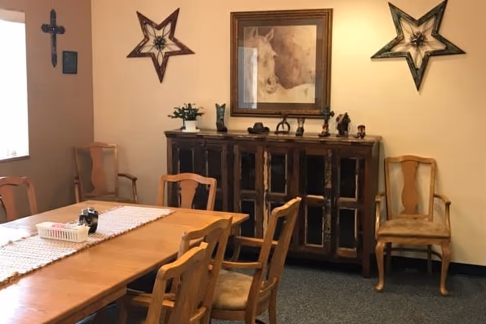 Dining room with a long wooden table and chairs, a rustic sideboard against the wall, and decorative wall art including stars and a framed horse print.