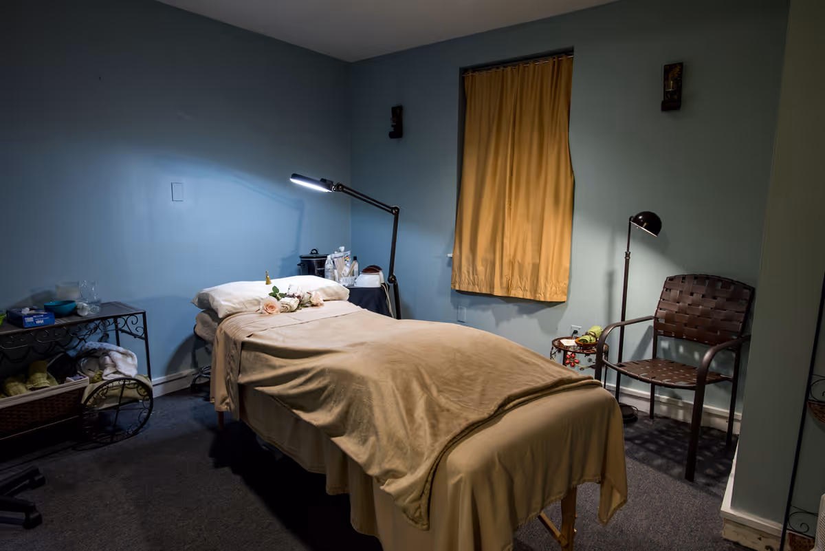 A teal-walled bedroom with a single bed, curtain, desk lamp, and wicker chair.