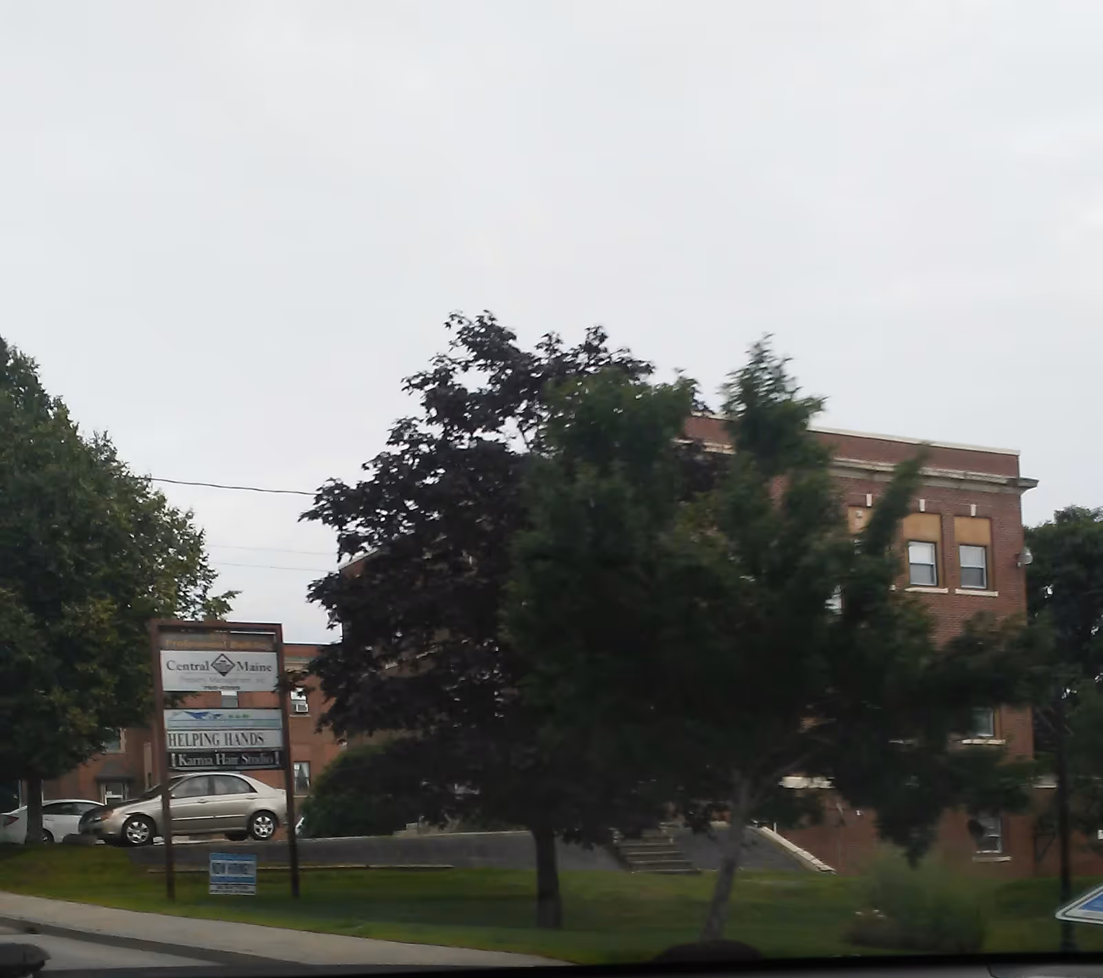 Brick senior living building with a Helping Hands sign and surrounding trees.