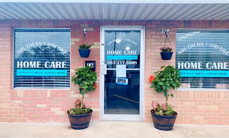 A brick storefront with a glass door, hanging planters, and large Home Care windows.