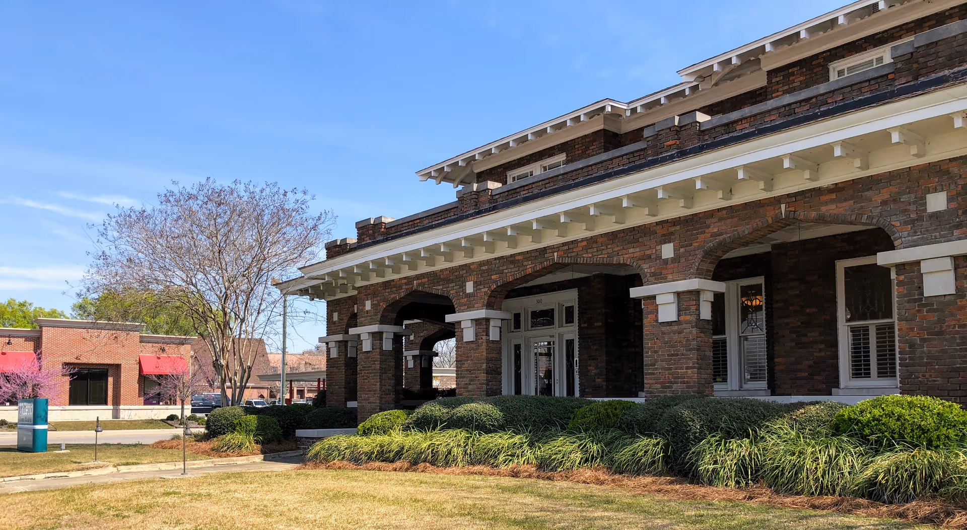 Exterior view of a brick senior living facility entrance with arches and manicured landscaping.
