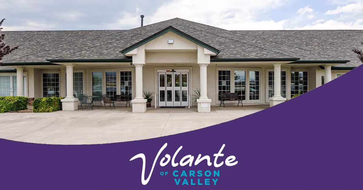 Front exterior view of Volante Senior Living of Carson Valley building with a covered entrance, multiple windows, benches, and some greenery.